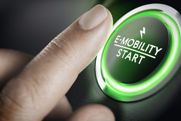 Man pushing green car button. Concept of e-mobility. Composite image between a hand photography and a 3D background.